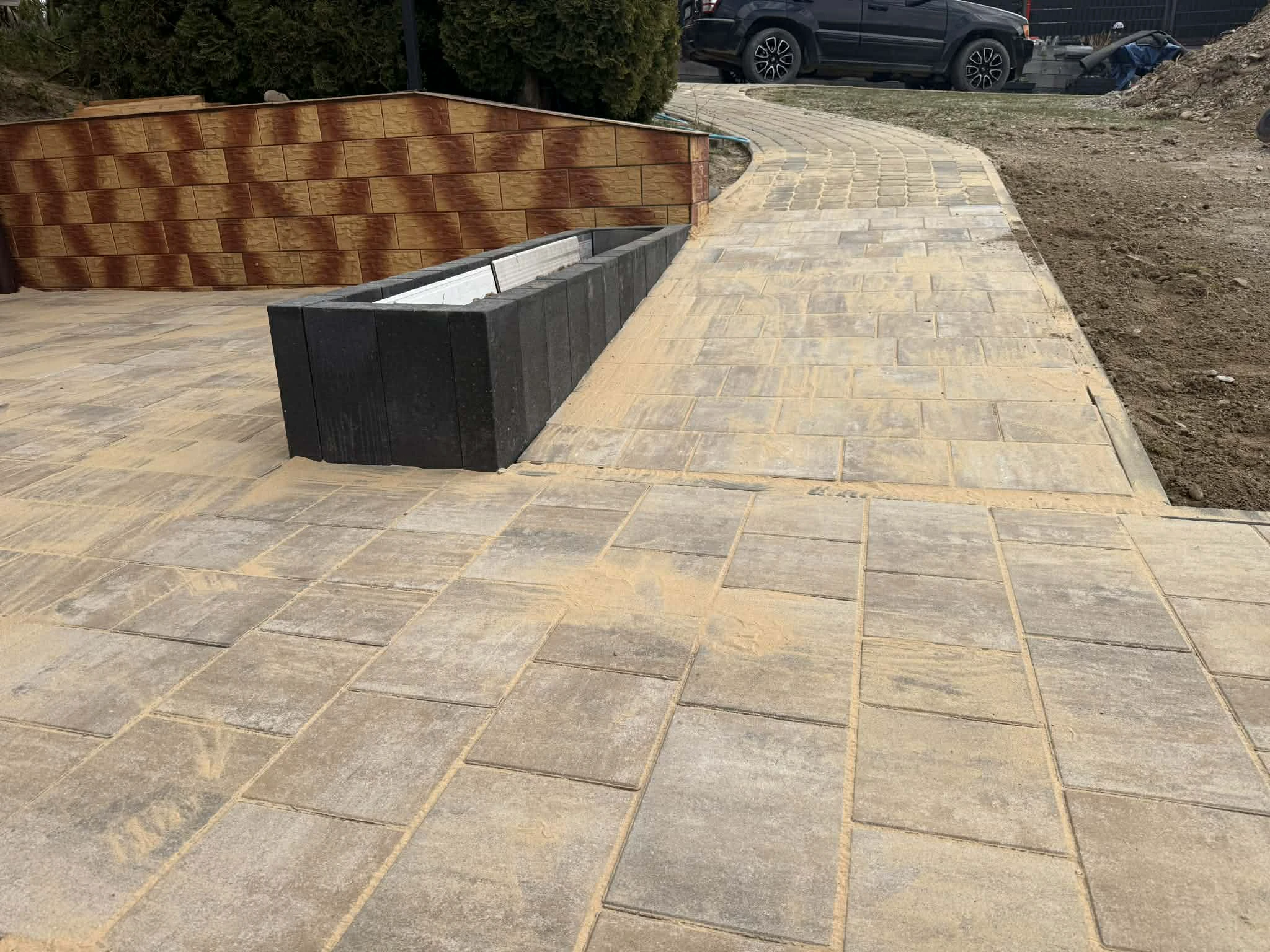 Chodnik z kostki brukowej na tle obramowania z czarnych palisad betonowych