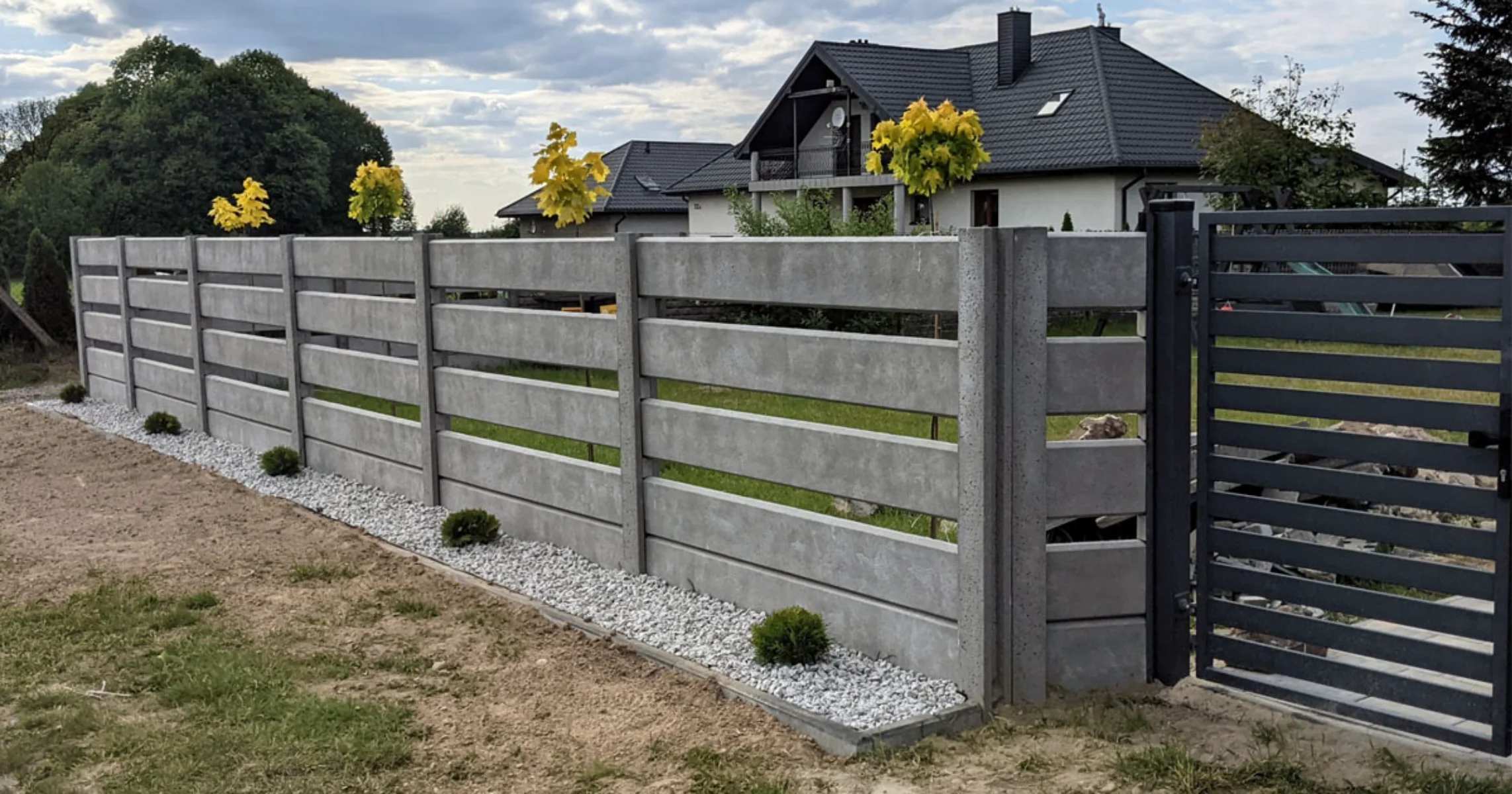 Ogrodzenie betonowe z prefabrykowanych płyt poziomych z opaską żwirową i furtką przy nowoczesnym domu